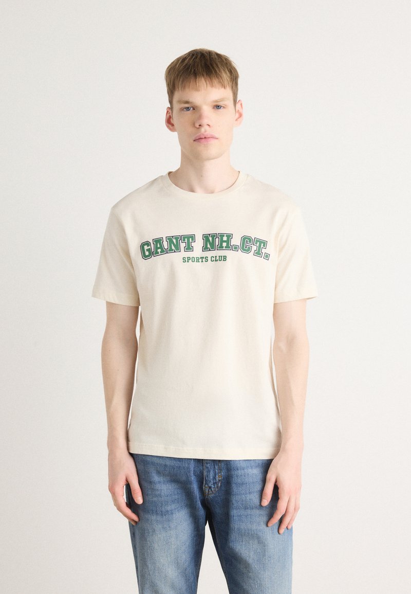 Cream-colored cotton t-shirt featuring a green printed text "GANT NH. CT. SPORTS CLUB," short sleeves, and a classic crew neck design.