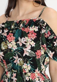 Květinové šaty s odhalenými rameny, černým pozadím, živými růžovými a bílými květy, volánkovým výstřihem a nastavitelnými tenkými ramínky.