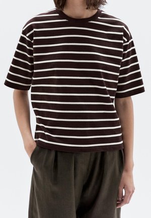 Brun- og hvidstribet kortærmet t-shirt lavet af blødt stof med rund hals og afslappet pasform. Kombineret med løse mørke bukser.