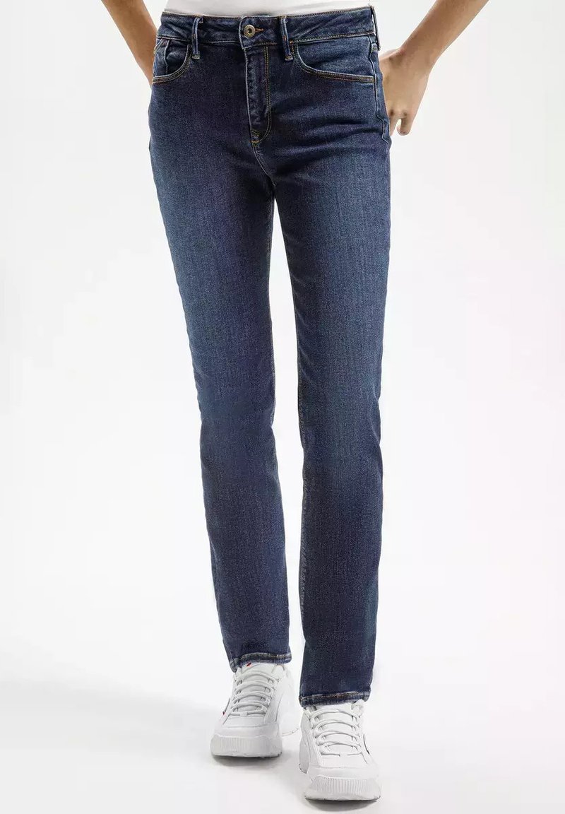 Slim fit granatowe dżinsy z pięcioma kieszeniami, zamkiem błyskawicznym i kontrastującymi pomarańczowymi stichami, w połączeniu z białymi sneakersami.