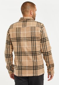 Beige flanellen shirt met zwart-wit ruitpatroon, lange mouwen, knoopmanchetten en een kraag. Zachte textuur en standaard pasvorm.