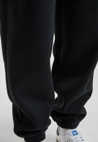 Mustad mustad teksad, mis on lõdva lõikega, elastsete mansettide ja siledaks tekstuuriga, koos valgete spordijalanõudega, millel on sinine logo.