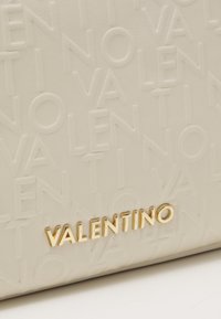 Krämfärgad läderpung med präglad "VALENTINO"-design och logotyp i guldton längst ner. Slät textur med en subtil lyster.
