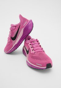 Paire de chaussures de course Nike roses avec logos swoosh noirs, tissu en maille et semelles violettes rembourrées sur fond blanc.