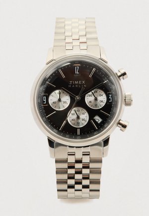 Timex Marlin kell musta sihvriga, hõbedast roostevabast terasest korpus ja rihm, kroonograafi subdialid ning suured araabia numbrilised tunni näidikud.