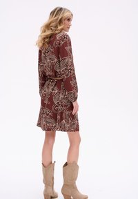 Br�ązowa sukienka z dużym kremowym kwiatowym i falistym wzorem, z długimi rękawami, w talii przewiązywana paskiem, o długości do kolan, w połączeniu z jasnobrązowymi kowbojkami.