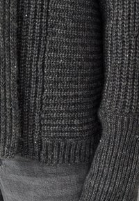 Donkergrijze gebreide trui met een geribbeld patroon, met een chunky ontwerp en subtiele pailletten die door de stof zijn geweven voor een lichte glans.