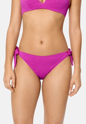 Mujer con bikini de color rosa brillante y textura, con nudos laterales, y top de bikini a juego, mostrado desde el abdomen hasta la mitad del muslo.