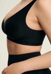 Black wireless bra with a smooth texture, plunging neckline, wide shoulder straps, and perforated design along the sides for breathability.