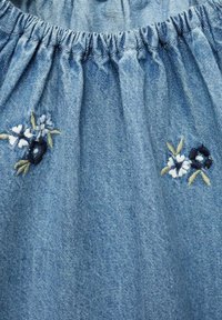 Denim material svetlo modre barve, z nabranim elastičnim pasom in cvetličnim vezenjem v beli, mornarsko modri in zeleni barvi.