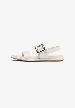 Sandales en cuir blanc avec une semelle plate, présentant une large sangle et un accent de boucle métallique sur la sangle de cheville. Texture lisse et design minimaliste.