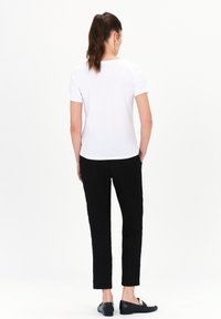 T-shirt bianca di cotone con maniche corte, abbinata a pantaloni neri slim-fit e scarpe nere slip-on. Texture liscia, design semplice.