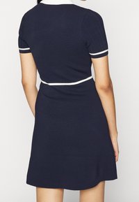 Granatowa sukienka krótko rękawowa z białym kołnierzykiem i detalami paska. Posiada żebrowane rękawy i rozkloszowany dół. Wykonana z miękkiego, teksturowanego materiału.