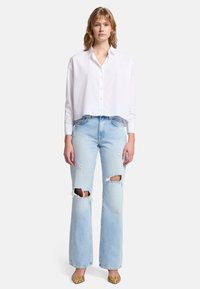 Hvid cropped skjorte med knaplukning, parret med lyseblå slidte bootcut jeans med knæhuller. Lette sko fuldender outfittet.
