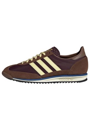 Brązowy i bordowy but Adidas z kremowymi paskami, beżowymi sznurowadłami, niebieskim wykończeniem na białej podeszwie i ryflowaną czarną podeszwą zewnętrzną.