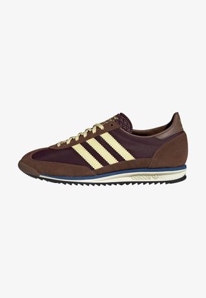 Brązowy i bordowy but Adidas z kremowymi paskami, beżowymi sznurowadłami, niebieskim wykończeniem na białej podeszwie i ryflowaną czarną podeszwą zewnętrzną.