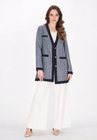 Marineblå og hvid vævet cardigan med v-hals-design, knaplukning og to forlommer. Accenteret med marineblå kant og knapdetaljer.