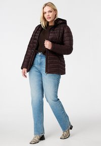 Bruine pufferjack met een capuchon, voorzien van een diagonaal quiltpatroon. Gecombineerd met lichtblauwe jeans en zwart-witte slangenprint enkellaarsjes.