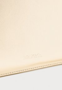 Superficie in pelle crema con logo "MAX&Co." in rilievo vicino al bordo cucito.