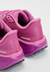 Paire de chaussures de sport roses avec tiges en tissu mesh, cols rembourrés et semelles en caoutchouc texturées, vues de dos et de côté.