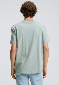 Jasnozielona koszulka z krótkim rękawem i okrągłym dekoltem. Miękka tkanina, luźny fason, prosty dół. Minimalistyczny design bez wzorów i logo.