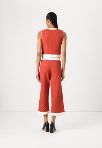 Rode textuur tweedelige outfit met een mouwloos topje en broek met wijde pijpen. Accenten met een witte tailleband en contrasterende witte zoom.