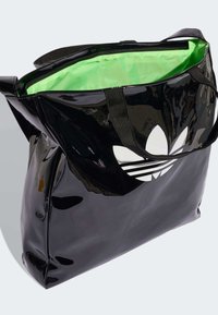 Black glossy tote bag with a white trefoil logo, featuring a bright green interior and black straps, showcasing a spacious design.