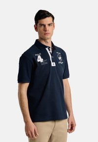 Polo náutico de algodón, con tapeta de dos botones, franjas acentuadas en blanco, un logotipo y el número '4' en el pecho.