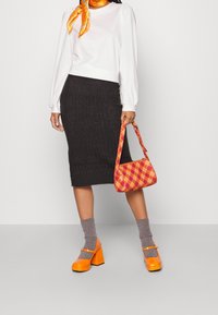 Maglietta bianca a maniche lunghe, gonna a tubo grigia a costine, borsa a scacchi arancione, scarpe Mary Jane arancioni in vernice e calze grigie a costine.