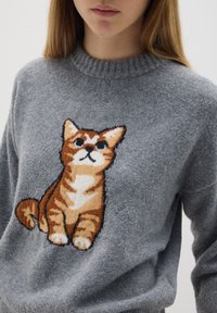 Grijs gebreid sweater met een afbeelding van een bruine tabby kat, met een ronde halslijn en ribgebreide manchetten, die de zachte textuur benadrukt.