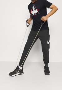 Camiseta Nike negra de manga corta con gráfico en rojo y blanco; pantalones de chándal negros con logo blanco de Nike; zapatillas deportivas negras con detalles en blanco.