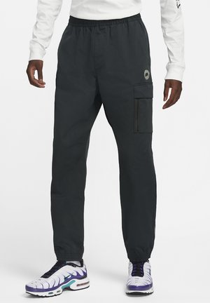 Schwarze Cargo-Hose mit elastischem Bund und Bündchen an den Knöcheln, getragen mit weißen und violetten Turnschuhen sowie einem weißen Langarmshirt.