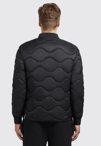 Black padded jacket with a wavy quilted design, ribbed cuffs, and a collar. Smooth texture, lightweight material, and minimalistic detailing.