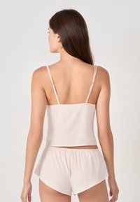 Canotta corta rosa pallido con spalline sottili e pantaloni coordinati, realizzata in un tessuto leggero e liscio, con un design semplice e pulito.