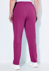 Pantaloni jogger fucsia con vita elastica. Realizzati in tessuto morbido, con una vestibilità slim e una superficie liscia. Sneakers bianche in vista.