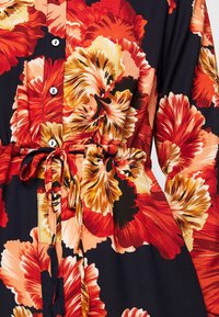 Abito floreale con un audace motivo rosso, arancione e crema su uno sfondo nero, con bottoni e una cintura regolabile in vita.