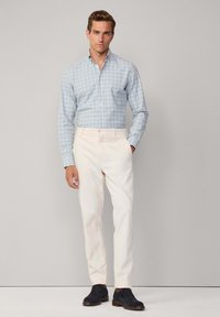 Checkered blue and white shirt, long sleeves, button-up design. Paired with cream-colored pants and navy lace-up shoes. Simple and clean look.