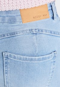 Svijetloplave traperice s vidljivim džepom i smeškim kožnim flasterom s natpisom "NOISY MAY" na pojasu. Također su vidljive šavova.