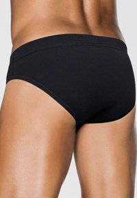 Uomo che indossa slip neri semplici, mostrati dalla vita fino alla parte superiore delle cosce, evidenziando la vista laterale e posteriore della biancheria intima.
