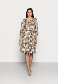 Vestido amarelo-bege com um padrão zig-zag castanho, mangas curtas, cintura atada e comprimento até ao joelho. Tecido suave, design minimalista.