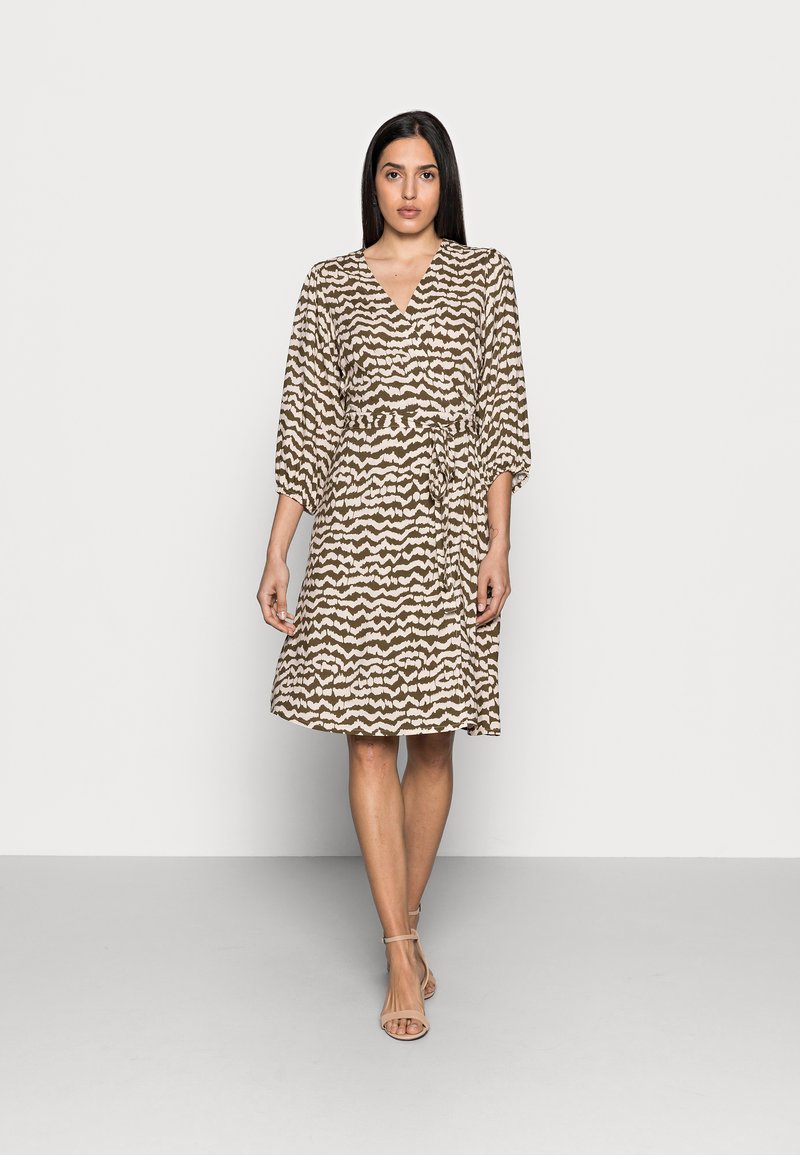 Vestido amarelo-bege com um padrão zig-zag castanho, mangas curtas, cintura atada e comprimento até ao joelho. Tecido suave, design minimalista.