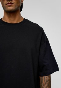 Zwarte katoenen t-shirt met een ronde hals, verlaagde schouders en korte mouwen. Glad textuur, minimale details.