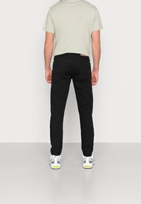 Czarne dżinsy o prostym kroju z wyhaftowanymi tylnymi kieszeniami i metką przy pasie. Połączone z jasnoszarym t-shirtem i białymi trampkami.