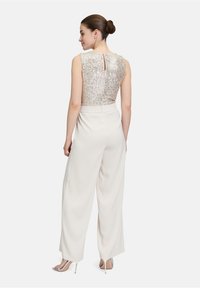 Biały kombinezon z bezrękawnikowym topem ozdobionym cekinami i dekoltem w kształcie łezki z tyłu, w zestawieniu z szerokimi spodniami i metalicznymi szpilkami.