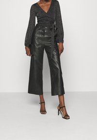 Svart långärmad omslagsblus med en texturerad lyster, i kombination med högmidjade vida läderbyxor. Svarta remsandaler med klack och en clutchtv.