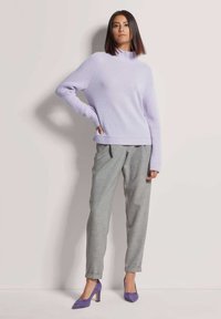 Lila gestrickter Pullover mit hohem Kragen und gerippten Ärmeln, kombiniert mit hellgrauen maßgeschneiderten Hosen und lila Wildleder-Pumps.