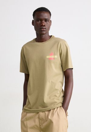 Camiseta de algodón caqui de manga corta, con cuello redondo y un logotipo impreso colorido en el lado izquierdo del pecho. Textura suave, ajuste relajado.