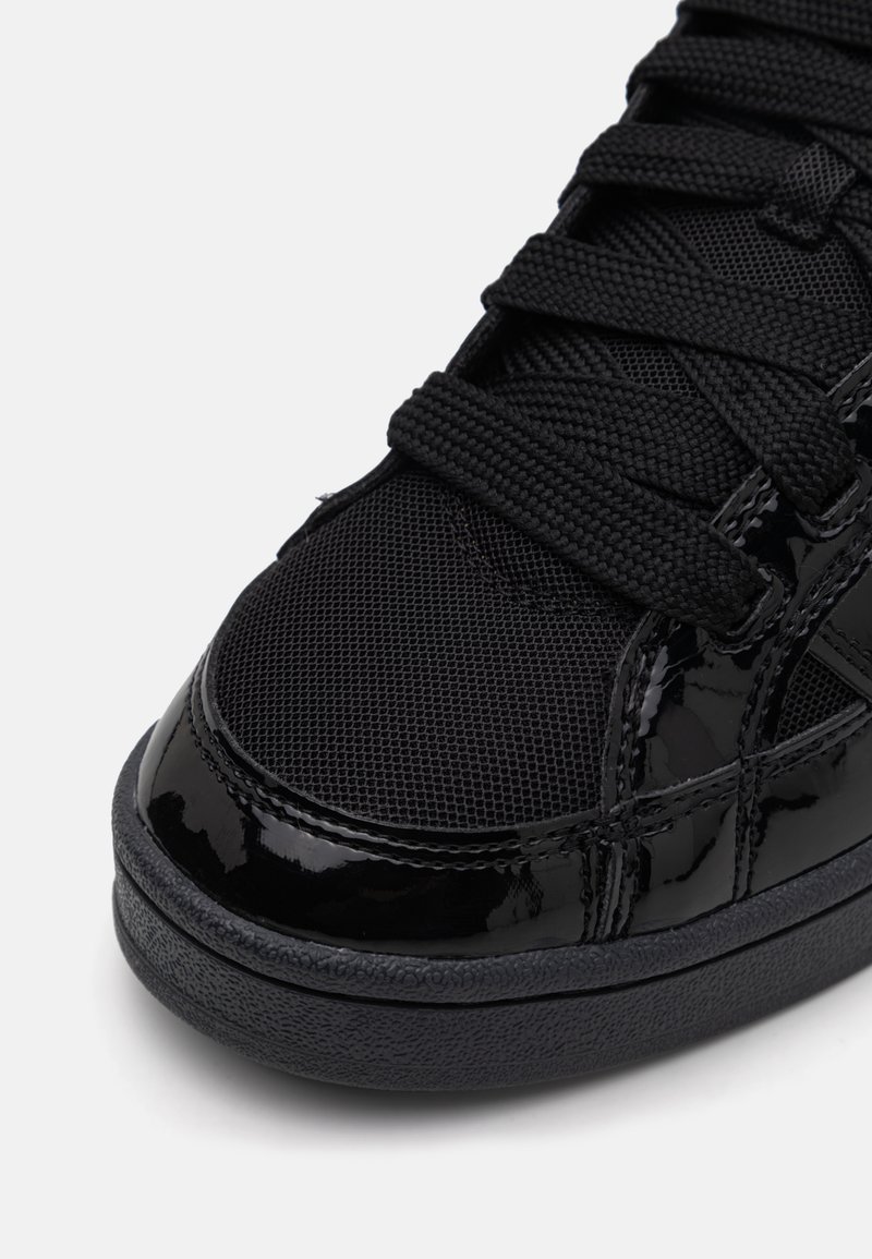 Zapatilla negra que presenta una combinación de malla y cuero sintético brillante, cordones texturizados y un diseño de punta redonda con una suave suela de goma negra.