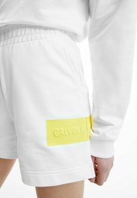 Bílé bavlněné šortky s elastickým pasem, bočními kapsami a fluorescentně žlutým akcentem s vyraženým logem "CALVIN KLEIN".