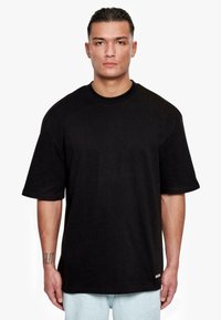 Black oversized short-sleeve T-shirt with a crew neck, made of cotton, featuring a subtle logo tag near the hem and a smooth texture.